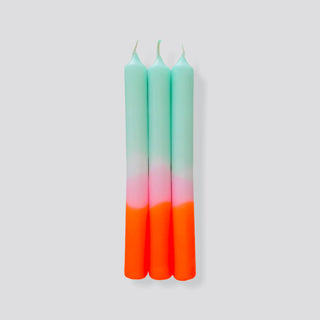 Drei handgefärbte Stabkerzen aus dem Set „Dip Dye Neon – Frühlingssorbet“ von Pink Stories liegen auf einem weißem Hintergrund.. Die Kerzen haben einen sanften Farbverlauf von Mintgrün über Rosé bis hin zu leuchtendem Neonorange.