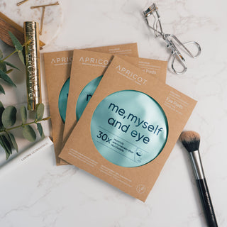 Wieverwendbare Augenpads mit Hyaluron der Marke Apricot Beauty & Healthcare in umweltfreundlicher Kartonverpackung, präsentiert auf einer marmorierten Oberfläche und dekoriert mit Eukalyptus und Kosmetikprodukten.
