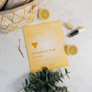 Wieverwendbare Decollete-Pad mit Vitamin C der Marke Apricot Beauty & Healthcare in umweltfreundlicher Kartonverpackung, präsentiert auf einer marmorierten Oberfläche und dekoriert mit Eukalyptus und Zitronen.