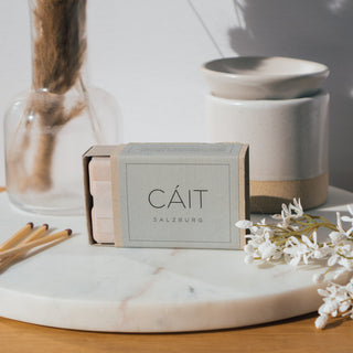 Duftwachswürfel der Sorte Bergamot, Blackcurrant & Birch von CAIT Salzburg, präsentiert auf einer Marmorplatte mit dekorativen Elementen, Streichhölzern und weißer Duftwachslampe.