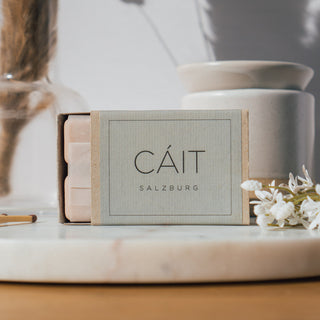 Duftwachswürfel der Sorte Bergamot, Blackcurrant & Birch von CAIT Salzburg, präsentiert auf einer Marmorplatte mit dekorativen Elementen, Streichhölzern und weißer Duftwachslampe.