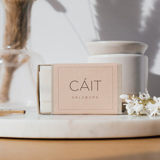 Duftwachswürfel der Sorte Lotusflower & Sandalwood von CAIT Salzburg, präsentiert auf einer Marmorplatte mit dekorativen Elementen und einer Duftwachslampe im Hintergrund.