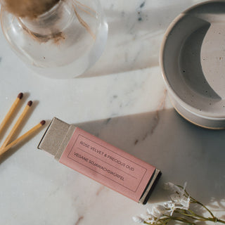 Duftwachswürfel der Sorte Rose Velvet & Precious Oud von CAIT Salzburg, präsentiert auf einer Marmorplatte mit dekorativen Elementen und einer Duftwachslampe daneben.