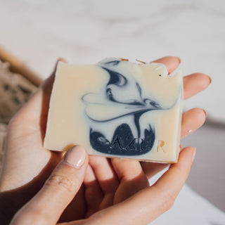 Handgemachte vegane Seife der Sorte Mighty Mint von Azur Natural Bodycare, die in den Händen einer Person gehalten wird, um die Details der Seife und das Logo zu zeigen.