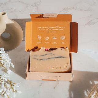 Handgemachte vegane Seife von Azur Natural Bodycare mit dem Namen Wildflower und den Duftnoten von Geranie und Grapefruit, präsentiert in eleganter Verpackung mit runder Vase und weißen Blumen im Hintergrund.