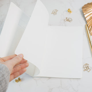 “Offene Innenseite eines minimalistischen Notizhefts von Typealive, mit weißem Papier, dezenten Details und umgeben von goldenen Büroaccessoires auf einer weißen Marmoroberfläche.