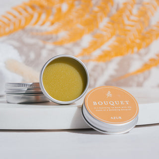 Handgemachter veganer Lippenbalsam der Sorte Bouquet von Azur Natural Bodycare, arrangiert auf einer Marmorplatte und orangenen Blättern im Hintergrund.