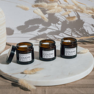 Mini-Duftkerzenset von Coudre Berlin mit den Sorten Bergamot & Patchouli, Koriander & Limette, und Rosmarin & Lavendel, präsentiert auf einer Marmorplatte mit dekorativen getrockneten Blumen im Hintergrund.