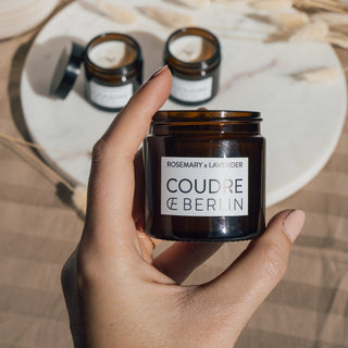Mini-Duftkerzenset von Coudre Berlin mit den Sorten Bergamot & Patchouli, Koriander & Limette, und Rosmarin & Lavendel, wird von einer Person in der Hand gehalten, im Hintergrund ist eine Marmorplatte und beiges Tuch.
