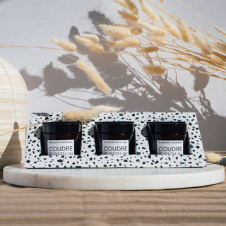 Mini-Duftkerzenset von Coudre Berlin mit den Sorten Bergamot & Patchouli, Koriander & Limette, und Rosmarin & Lavendel, präsentiert auf einer Marmorplatte mit dekorativen getrockneten Blumen im Hintergrund.
