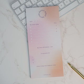 Moderner Notizblock „Daily Tasks“ von Typealive mit sanftem Pastellverlauf in Rosa und Beige, platziert auf einem Schreibtisch neben einer Tastatur und einem goldenen Stift. Perfekt für tägliche Aufgaben, Affirmationen und Dankbarkeitsnotizen.
