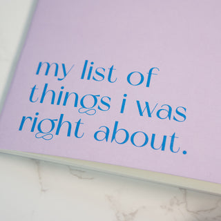 Detailaufnahme des Notizhefts ‘Right About’ in Fliederfarben von Typealive, mit der blauen Aufschrift ‘my list of things i was right about’, auf einer weißen Marmoroberfläche.