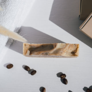 Handgemachte vegane Peelingseife der Sorte Coffee Comfort von Azur Natural Bodycare, präsentiert mit Kaffeebohnen und einem Handtuch von oben fotografiert.