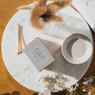 Produktübersicht der Duftwachswürfel von CAIT Salzburg in den Sorten Bergamot, Birch & Blackcurrant, Lotus Flower & Sandalwood, und Rose Velvet & Precious Oud, präsentiert auf einer Marmorplatte mit dekorativen Elementen und Streichhölzern.
