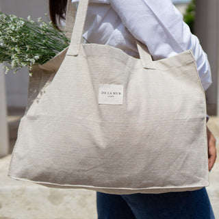 Stofftasche Everyday Bag M im Muster Natural Linen von De La Mur, getragen von einer Person, die einen Blumenstrauß in der Tasche hat, vor einer hellen Säulenstruktur.