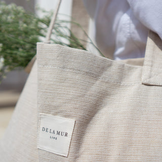 Stofftasche Everyday Bag M im Muster Natural Linen von De La Mur, Nahaufnahme des beigen Stoffes mit Blumen und Bluse im Hintergrund.