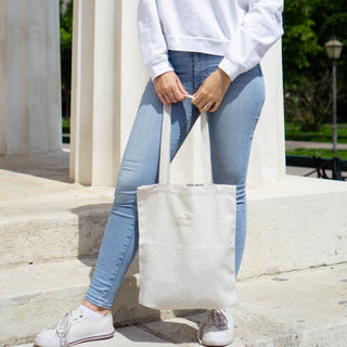 Frau hält eine Stofftasche Shopper M in der Farbe Chevron Cream von De La Mur, während sie in Jeans und weißen Sneakern vor einer Säule steht.