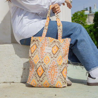 Frau sitzt mit einer Stofftasche Shopper M in der Farbe Vibrant Ikat von De La Mur, im Freien vor einer Säule.