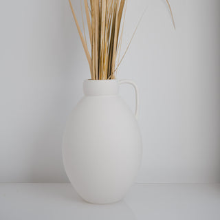 Minimalistische Vase Ghara groß, handgefertigt von Claet. Elegantes Design mit sanft gerundeter Form und praktischem Griff, perfekt für zeitgenössische Dekorationen oder Trockenblumenarrangements. Gefertigt in hochwertigem, strukturiertem Weiß.