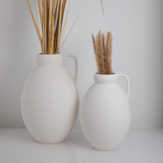 Minimalistische Vase Ghara groß und klein, handgefertigt von Claet. Elegantes Design mit sanft gerundeter Form und praktischem Griff, perfekt für zeitgenössische Dekorationen oder Trockenblumenarrangements. Gefertigt in hochwertigem, strukturiertem Weiß.