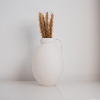 Minimalistische Vase Ghara klein, handgefertigt von Claet. Elegantes Design mit sanft gerundeter Form und praktischem Griff, perfekt für zeitgenössische Dekorationen oder Trockenblumenarrangements. Gefertigt in hochwertigem, strukturiertem Weiß.