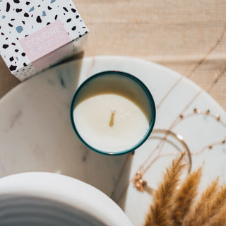 Vegane Duftkerze der Sorte Verbena & Neroli von Coudre Berlin, präsentiert von oben in einem grünen Glasgefäß neben der Verpackung auf einer Marmorplatte mit dekorativen Elementen im daneben.