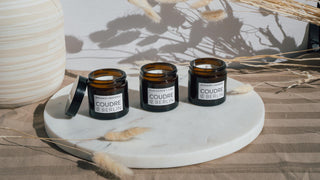 Mini-Duftkerzenset von Coudre Berlin mit den Sorten Bergamot & Patchouli, Koriander & Limette, und Rosmarin & Lavendel, präsentiert auf einer Marmorplatte mit dekorativen getrockneten Blumen im Hintergrund.