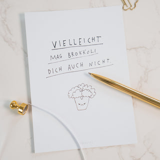 Postkarte mit der humorvollen Aufschrift ‘Vielleicht mag Brokkoli dich auch nicht’ und einer gezeichneten Brokkoli-Illustration, dekoriert mit einem goldenen Kugelschreiber und goldenen Büroklammern, auf einem Marmorhintergrund, von Typealive.